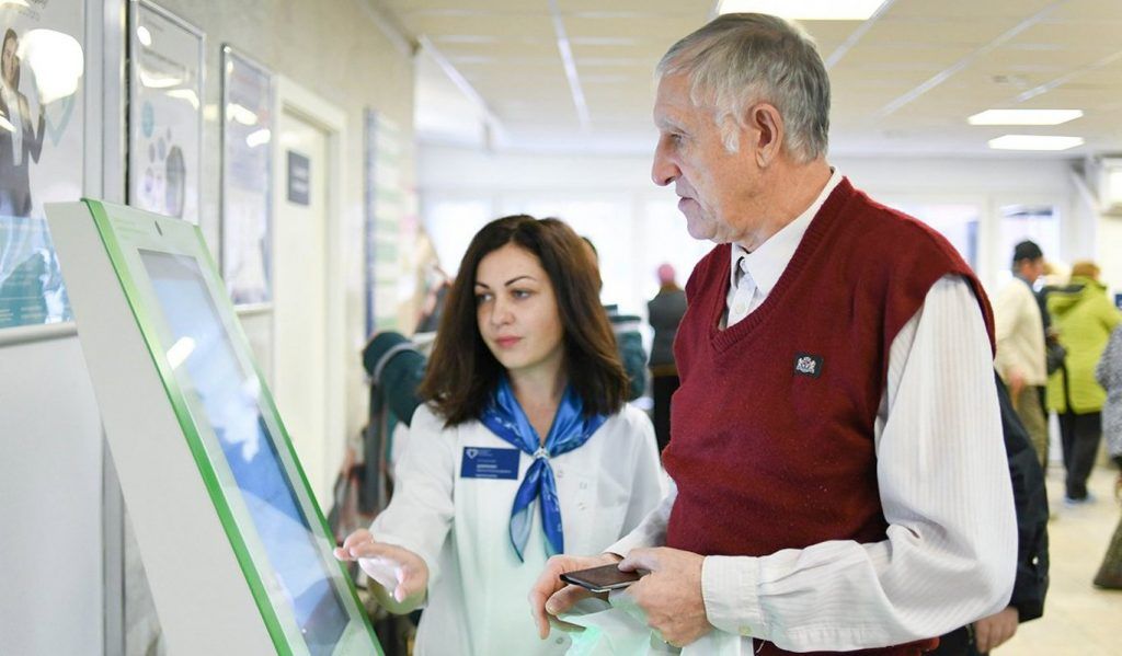 Сотрудница поликлиники помогает пациенту распечатать талон для приема к врачу 17 мая 2019 года. Фото: сайт мэра Москвы