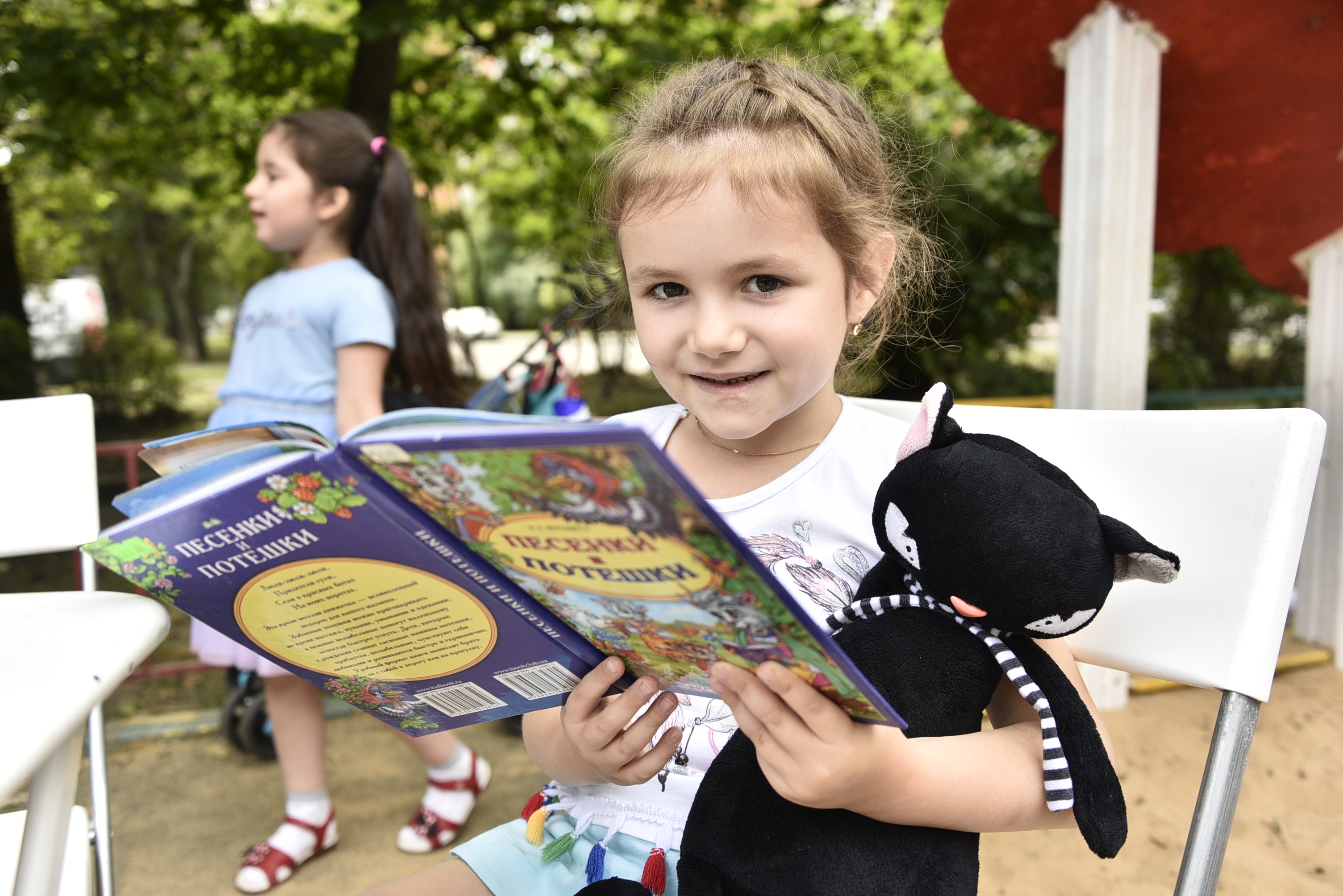5 августа 2020 года. Участница летней читальни на Каширском, пятилетняя Карина Валуйская, очень любит кошек — и на празднике читала книжку вместе с игрушечным черным котом. Фото: Пелагия Замятина